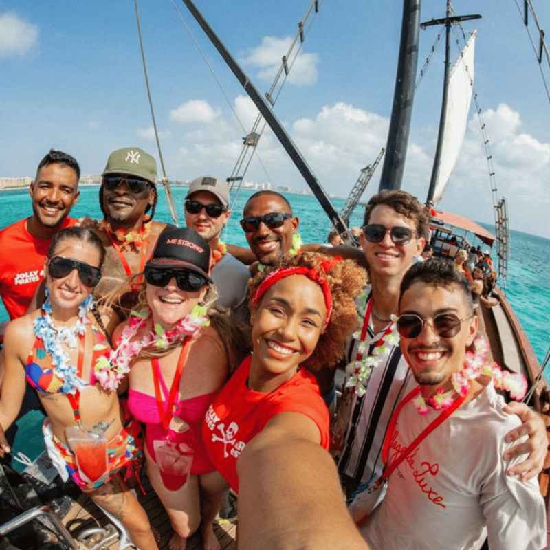 Group of people smiling on a sailboat with blue ocean and sky in the background.