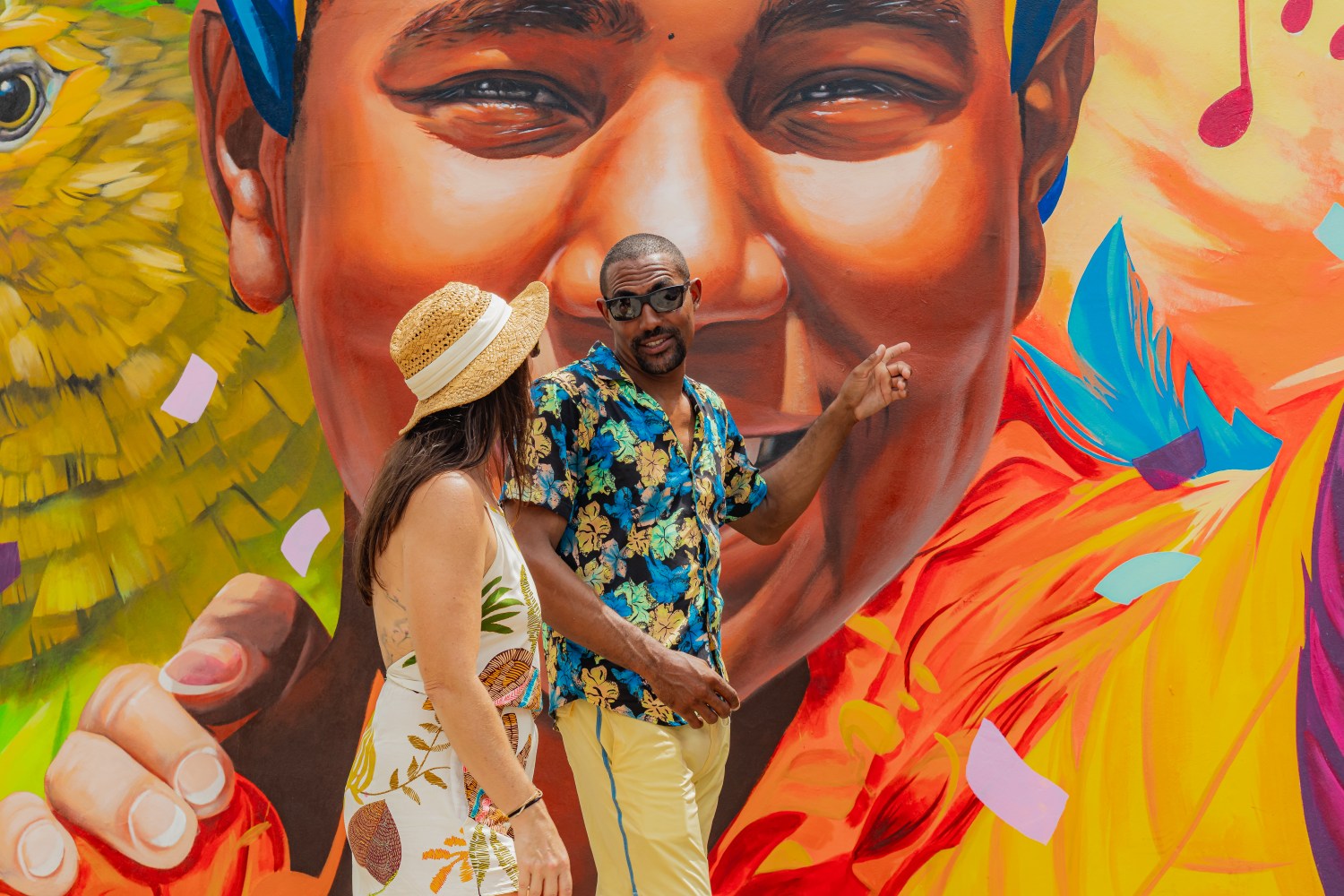 Two people in front of a colorful mural with a smiling face.
