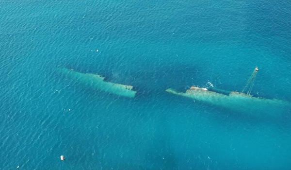 Aerial view of a partially sunken ship in clear blue water.