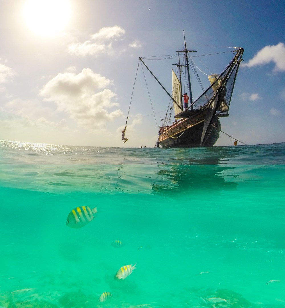 Ship on ocean with fish swimming underwater, sunny sky.