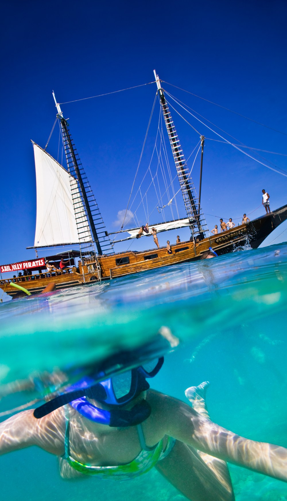 Person snorkeling underwater near a sailing ship on a clear day.